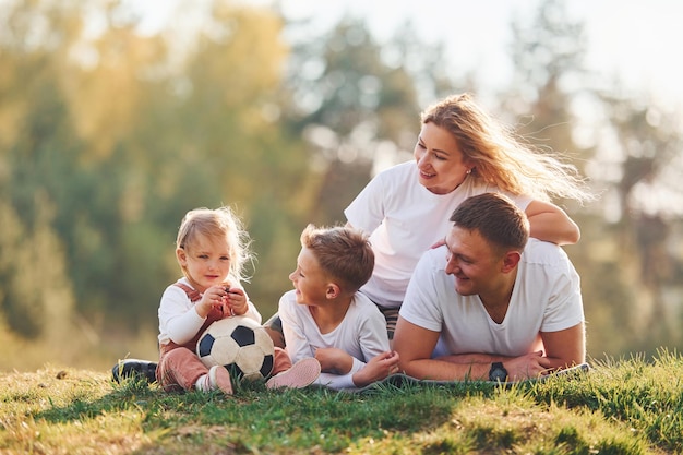 Com bola de futebol família feliz deitada ao ar livre perto da floresta com filha e filho