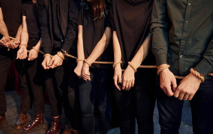 Foto com corda nas mãos grupo de atores em roupas de cor escura em ensaio no teatro