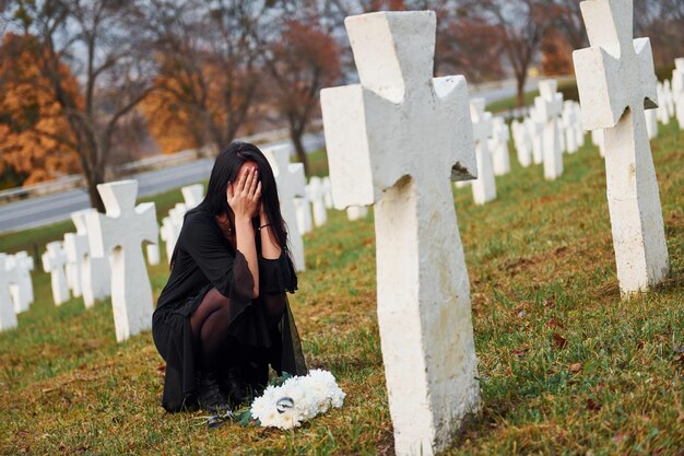 Foto com flores nas mãos jovem de roupas pretas visitando o cemitério com muitas cruzes brancas concepção de funeral e morte