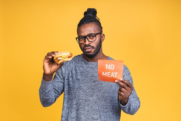 Com fome jovem afro-americano negro comendo hambúrguer isolado sobre fundo amarelo. Conceito de dieta. Conceito vegan ou vegetariano.