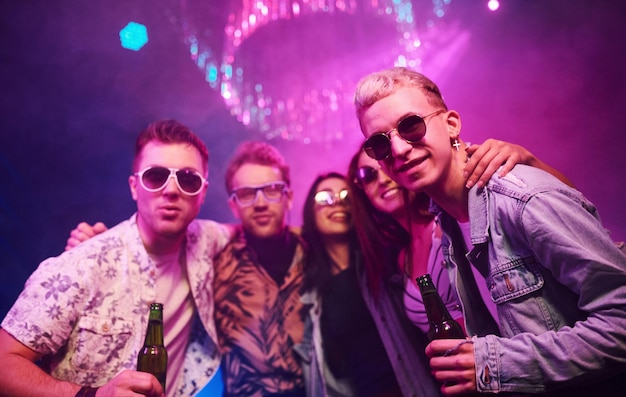 Foto com garrafas de cerveja nas mãos jovens está se divertindo na boate com luzes laser coloridas