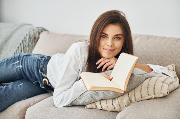 Com livro linda jovem de jeans e camisa branca está em casa