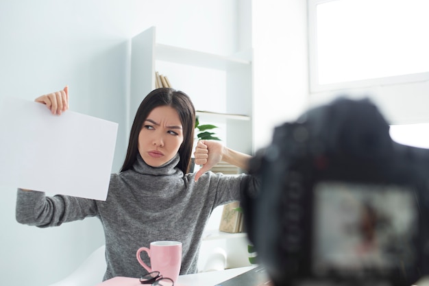 Com raiva blogueiro feminino está sentado à mesa e gravação de vídeo