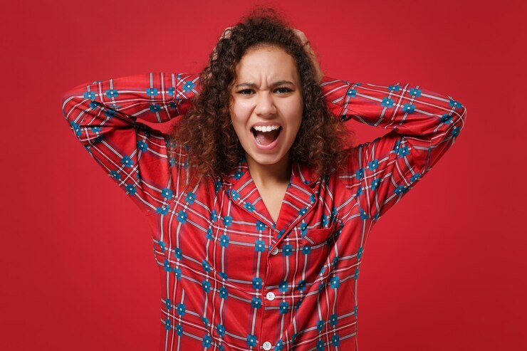 Foto com raiva jovem afro-americana em homewear de pijama posando descansando em casa isolada em fundo vermelho no estúdio. relaxe o conceito de estilo de vida de bom humor. mock up espaço de cópia. coloque as mãos na cabeça, gritando.