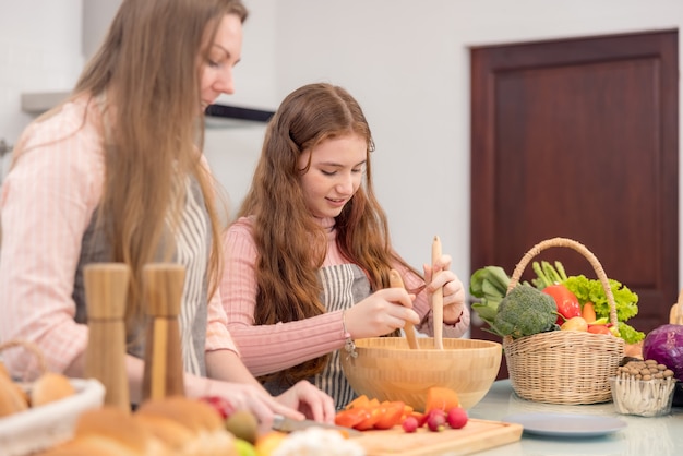 Com sua mãe, uma jovem está aprendendo a preparar um jantar. preparar refeições saudáveis. Na cozinha, uma família feliz. As verduras e frutas estão sendo preparadas pela mãe e sua filha.