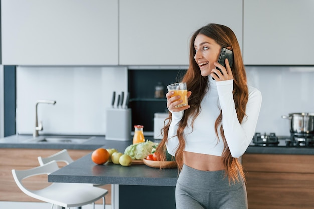 Com suco de laranja fresco A jovem europeia está dentro de casa na cozinha com comida saudável