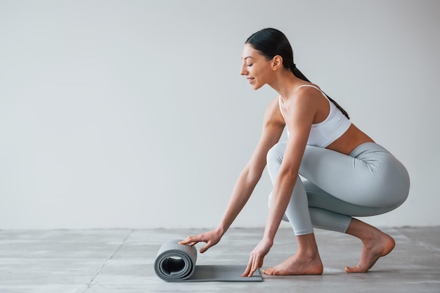 Com tapete de ioga Mulher com tipo de corpo magro esportivo em roupas íntimas que está no estúdio