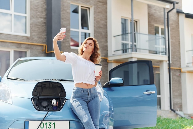 Foto com telefone jovem em roupas casuais com seu eletromóvel ao ar livre durante o dia