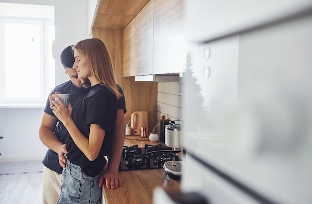 Com um copo de bebida fresca. Manhã para o jovem casal que está dentro de casa na cozinha.