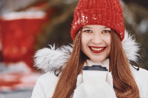 Com um copo de bebida nas mãos jovem feliz em pé ao ar livre e comemorando as férias de natal