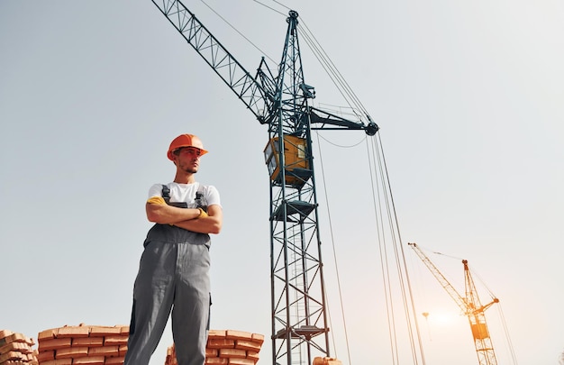 Com um guindaste ao fundo, um jovem trabalhador da construção em uniforme está ocupado no edifício inacabado.