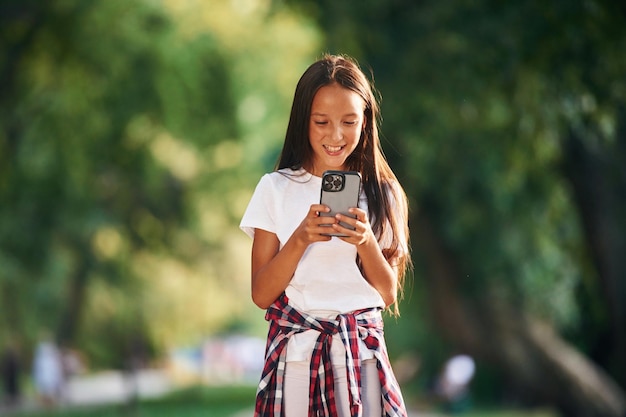 Com um smartphone, uma jovem vestida casualmente está no parque público ao ar livre.