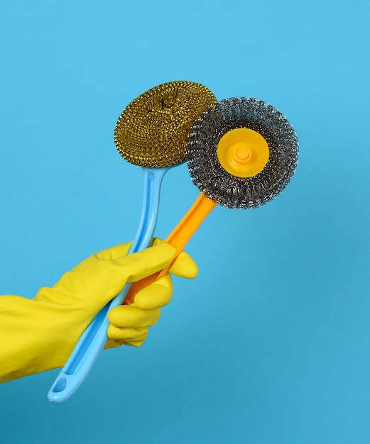 Com uma luva amarela segurando uma pilha de escovas de limpeza de plástico