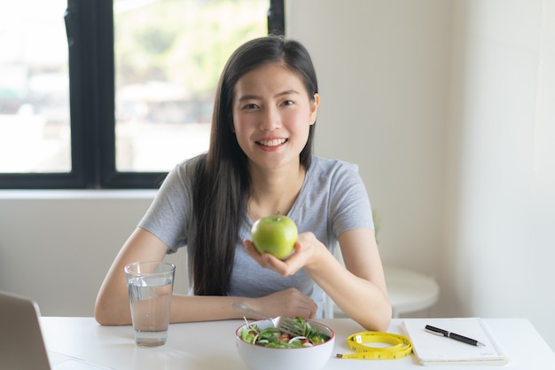 Foto coma alimentos saludables en el estilo de vida de bienestar. mujer joven de la belleza que sostiene la manzana verde en su mano y que come una ensalada.