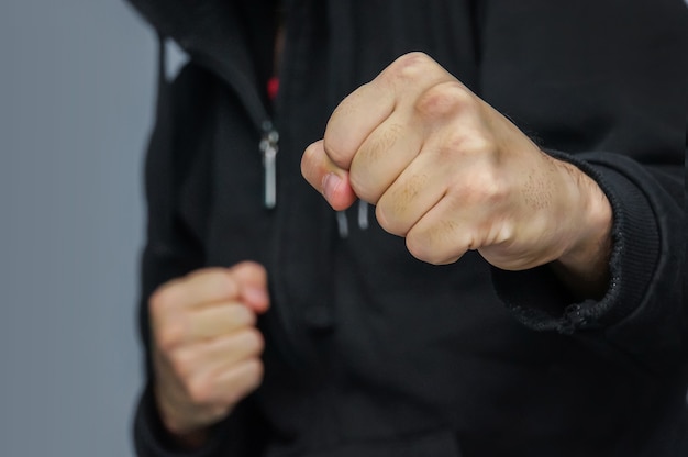 Foto combate mão-a-mão. lutador de rua. close-up do punho masculino. lutador com um capuz preto se prepara para atacar com o punho.