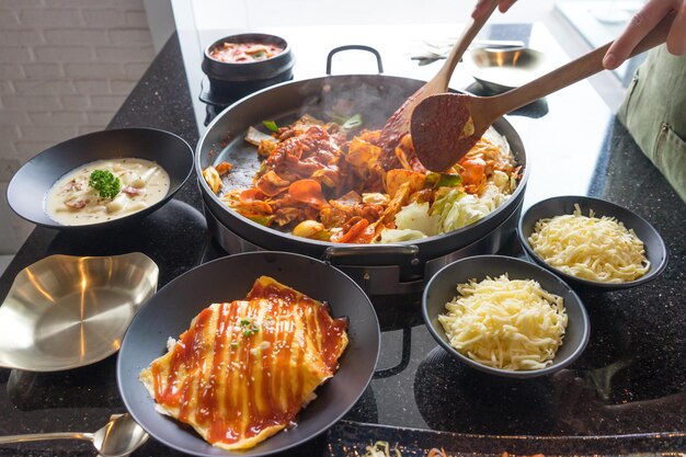 Combinación de pastel de arroz picante y picante de comida tradicional coreana Tokboki y aplicación de hojaldre con queso y vegetales en la mesa negra