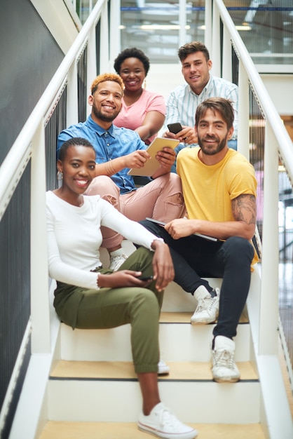 La combinación perfecta de diferentes habilidades comerciales Retrato de un grupo de jóvenes empresarios confiados sentados en los escalones de una oficina moderna