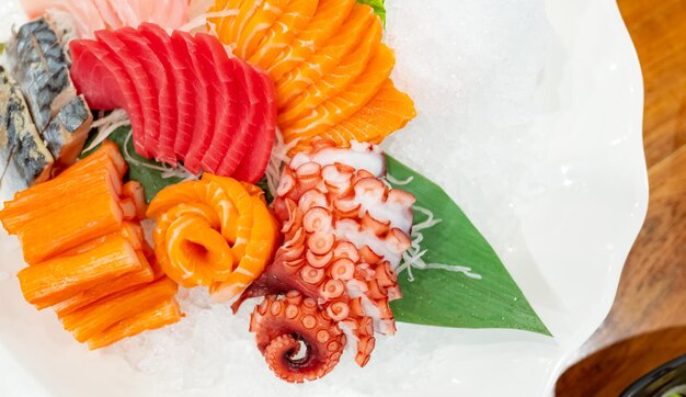 Foto combo de comida japonesa salmão, atum, sashimi, polvo gigante e bastões de caranguejo servidos com gelo triturado em prato branco na mesa do restaurante carne de peixe cortada em fatias buffet de frutos do mar comida japonesa saudável