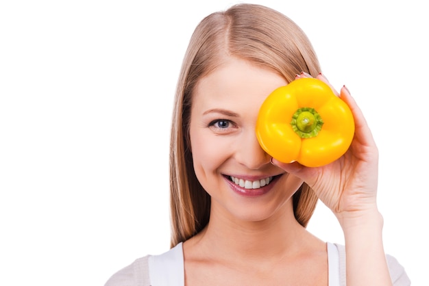 ¿Come alimentos saludables? Hermosa joven tapándose los ojos con ensalada de pimiento y sonriendo mientras está de pie contra el fondo blanco.