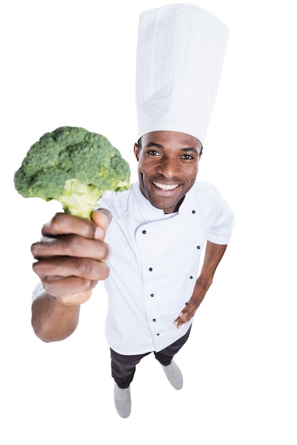 ¡Come sano! Vista superior del alegre joven chef africano en uniforme blanco estirando brócoli