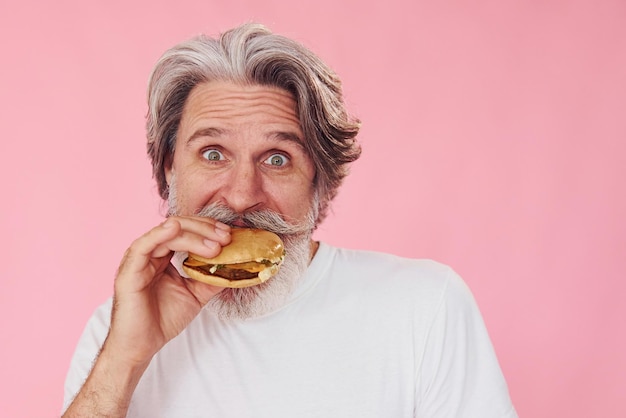 Come um delicioso hambúrguer Homem moderno e elegante com cabelos grisalhos e barba está dentro de casa