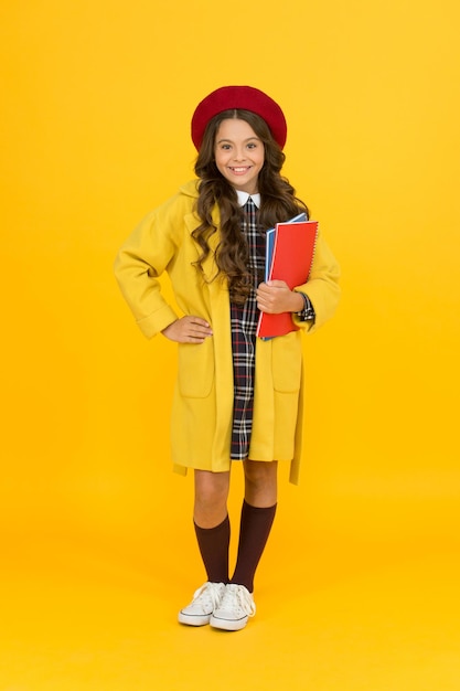 Começando o ano de estudo elegante adolescente estudante universitária garotinha com notebook ou pasta de trabalho para a escola de educação de lição e criança de moda em uniforme de aluno criança em boina francesa em fundo amarelo