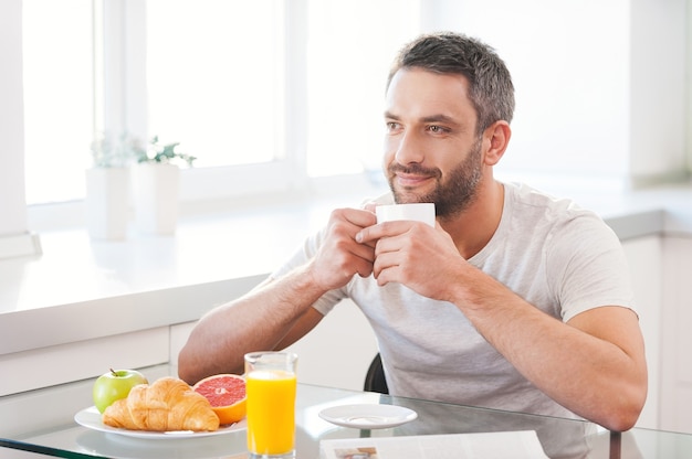 Começando o dia com um café fresco e quente. Jovem bonito tomando café fresco enquanto está sentado na cozinha