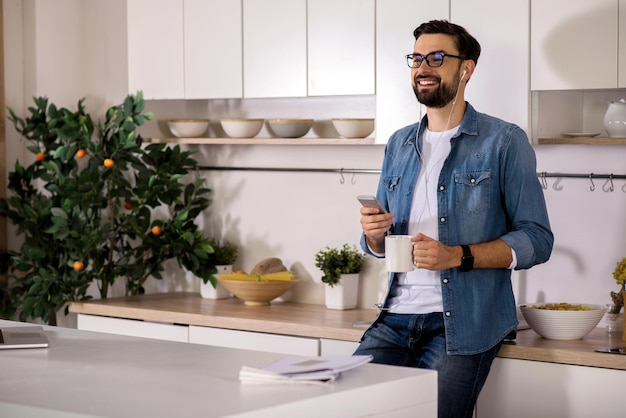 Comece o seu dia Jovem positivo parado na cozinha e bebendo chá enquanto ouve música