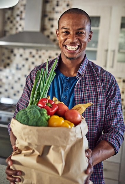 Comecei a comer mais saudável Retrato recortado de um jovem bonito segurando uma sacola de compras na cozinha em casa