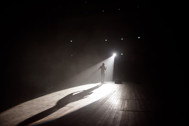 Comediante de pie en el escenario bajo el rayo de luz.
