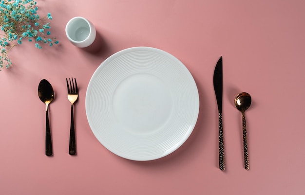 Comedor preparado con plato vacío y cuchillo y tenedor listos sobre fondo rosa