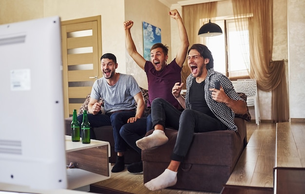 Comemorando a vitória. Empolgados três amigos assistindo futebol na TV em casa juntos.
