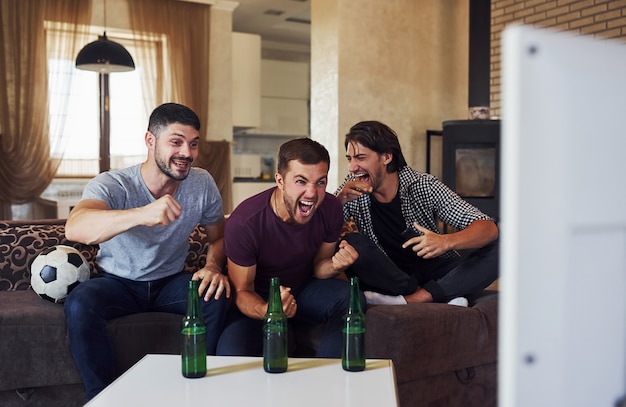 Foto comemorando a vitória. empolgados três amigos assistindo futebol na tv em casa juntos.