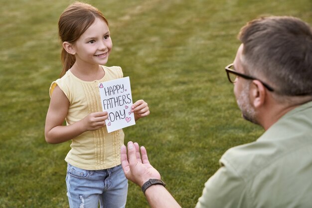 Comemorando o dia dos pais feliz ao ar livre linda garotinha sorridente dando a seu pai