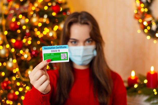 Comemorando o Natal durante a pandemia de coronavírus Retrato de uma jovem mostrando o certificado de vacinação contra o coronavírus para a câmera em pé decorado para a sala de Natal