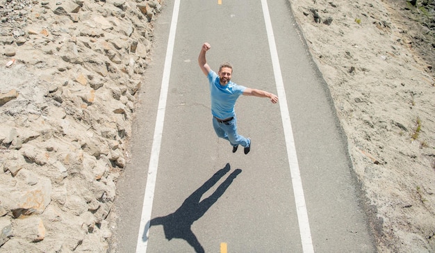 Comemorando o sucesso, homem maduro, pulando na estrada cheia de energia, cara feliz, sente liberdade