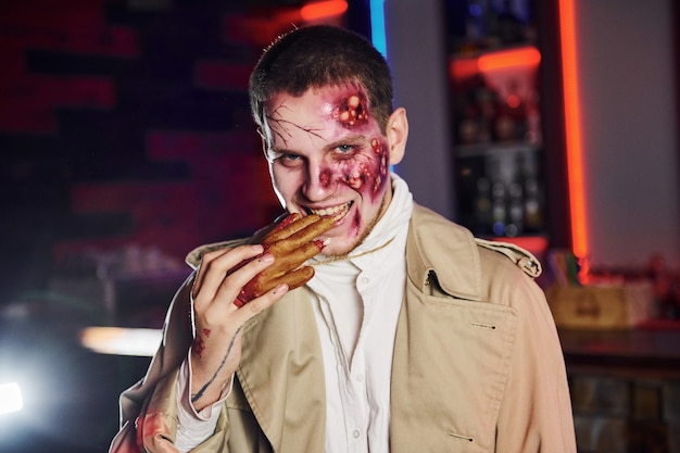 Comendo a mão morta. Retrato de homem que está na festa de halloween temática em fantasia e maquiagem de zumbi.