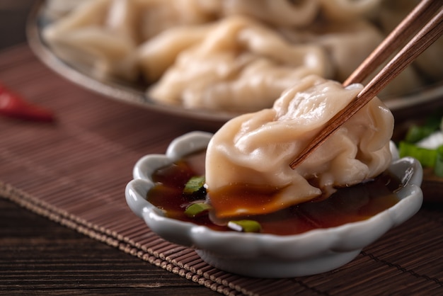 Comendo bolinhos cozidos frescos e deliciosos, jiaozi no fundo da mesa de madeira com molho de soja