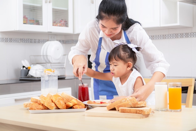 Comendo e conceito dos povos - mãe feliz e filha asiáticas que comem o café da manhã em casa.