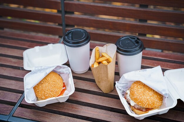 Foto comendo grande hambúrguer cheeseburgerbatatas fritascafé comida de rua saborosa e gordurosa take away burgerpausa para almoço ao ar livre no parque sentado no bancodieta pouco saudávelrelaxamento de fim de semanaproblemas de excesso de peso