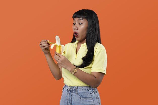 Comendo o conceito de frutas. Retrato engraçado e alegre de mulher asiática com banana em fundo colorido
