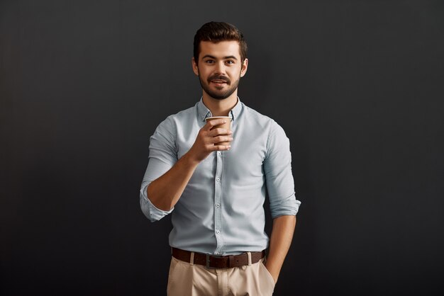 Comenzando un nuevo día alegre joven barbudo sosteniendo una taza de café caliente y mirando