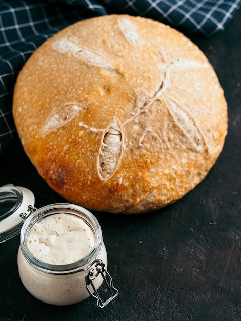 Comenzante de lechuga y pan de lechuga de trigo Comenzante de lechuga de trigo en frasco de vidrio y pan de lechuga redondo casero en fondo negro espacio de copia concepto de fabricación de pan de lechuga casera vertical