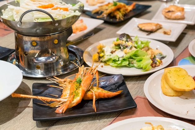 Comer camarones picantes a la parrilla con mucha comida en una mesa de madera