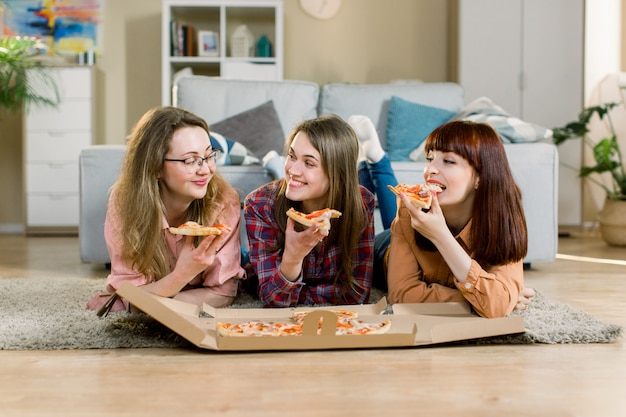 Foto comer comida rápida. felices tres hermosas amigos riendo, comiendo pizza en casa fiesta. mujeres cenando juntas, disfrutando de la comida. ocio, amistad, celebración y concepto de personas