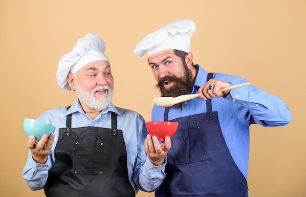 Comer concepto. Cocineros de restaurante profesionales de hombres barbudos maduros. Deliciosa receta. El equipo de cocina prepara la comida. Tradición familiar. Hombres chef cocinando. Dinastía culinaria. Enseñanza culinaria. Libro culinario.