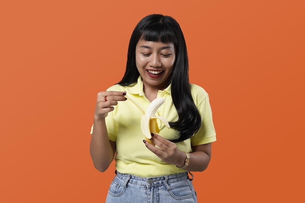 Comer concepto de fruta. Retrato divertido y alegre de mujer asiática con plátano sobre fondo colorido