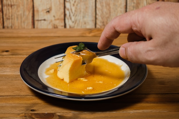 Comer el delicioso postre típico argentino y sudamericano llamado Flan con caramelo. Se observa la mano del comensal. Concepto de alimentación saludable y natural.