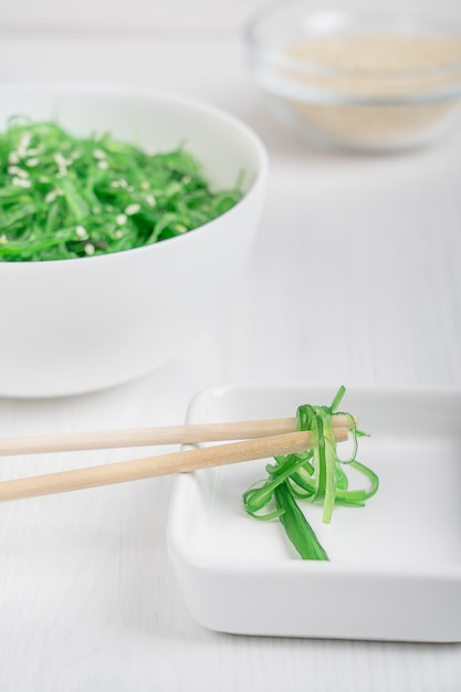 Comer ensalada de algas chuka wakame con semillas de sésamo servido en platillo blanco con palillos de bambú