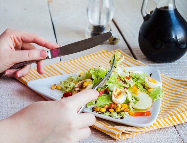 Comer ensalada verde con huevos de codorniz, maíz y manzana, mano, tenedor y cuchillo